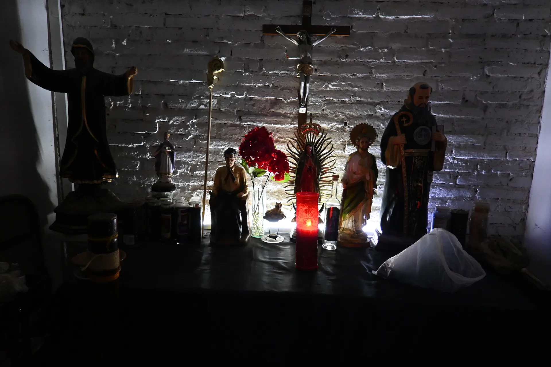 Altar religioso con santos, crucifijo y velas en ambiente oscuro